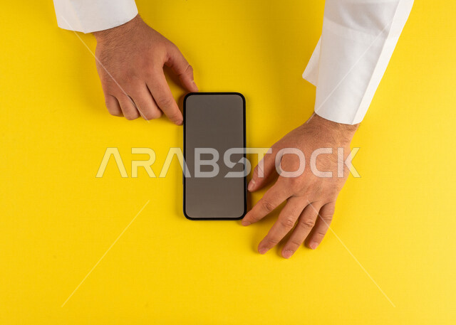 صورة مقربة ليد رجل عربي خليجي سعودي يستخدم الهاتف المحمول ،ايماءات اليد تدل على عرض مواصفات الجهاز،بيع وشراء الهاتف المحمول ،الترويج لتطبيق الكتروني ، التسويق لموقع ويب ، اجراء مكالمات فيديو