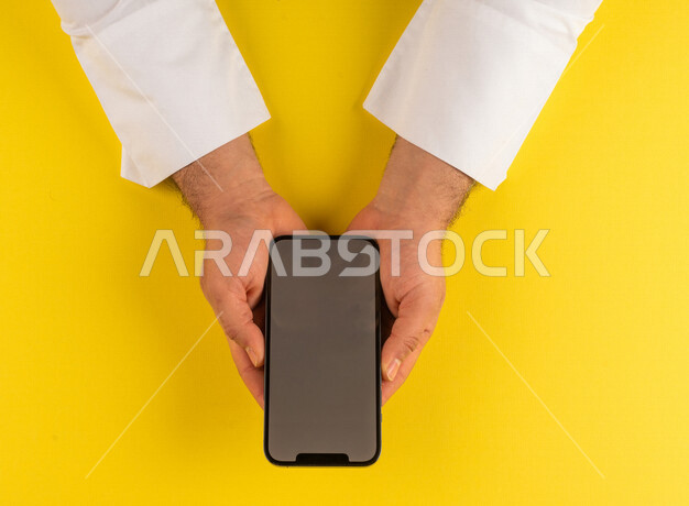 صورة مقربة ليد رجل عربي خليجي سعودي يستخدم الهاتف المحمول ،ايماءات اليد تدل على عرض مواصفات الجهاز المحمول ،الترويج لتطبيق الكتروني ، التسويق لموقع ويب ، اجراء مكالمات فيديو