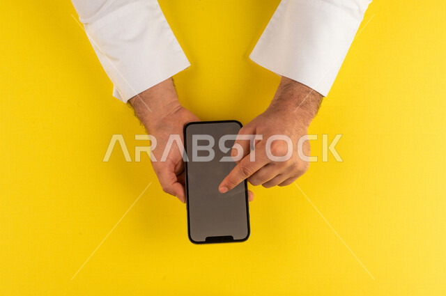 صورة مقربة ليد رجل عربي خليجي سعودي ينقر على شاشة الهاتف المحمول ، التسويق الالكتروني، تصفح المواقع الالكترونية ،تحديد الموقع ، العاب الكترونية ،ستخدام الاجهزة التقنية الحديثة في الاعمال الادارية
