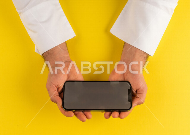 صورة مقربة ليد رجل عربي خليجي سعودي يحمل الهاتف المحمول ، الاستمتاع بمشاهدة الافلام ، لعب الالعاب الالكترونية ، متابعة الدروس التعليمية ،استخدام التقنيات الحديثة
