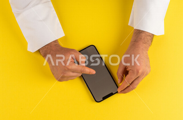 صورة مقربة ليد رجل عربي خليجي سعودي ينقر على شاشة الهاتف المحمول ، التسويق الالكتروني، تصفح المواقع الالكترونية ،تحديد الموقع ، العاب الكترونية ،ستخدام الاجهزة التقنية الحديثة في الاعمال الادارية