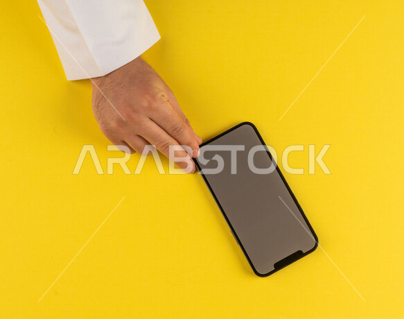 صورة مقربة ليد رجل عربي خليجي سعودي يضع يده على الهاتف المحمول ، ايماءة اليد تدل على اعطاء الهاتف لشخص، بيع وشراء الهاتف المحمول ،الترويج لتطبيق الكتروني ، التسويق لموقع ويب
