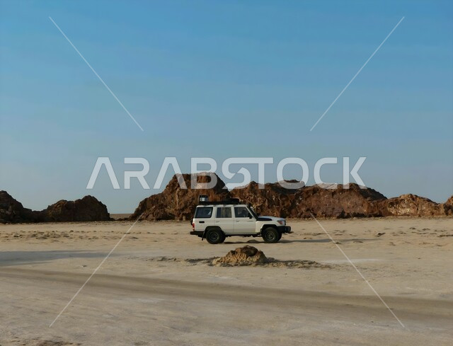 التشكيلات والتكوينات الصخرية، سيارة تويوتا لاند كروزر بيضاء تتجول وسط الصحراء العربية، التضاريس القاسية والطبيعة الجبلية، الكثبان والتلال الرملية في المناطق الصحراوية، مغامرات ورحلات السفاري في الصحاري الواسعة، الرمال الذهبية اللامعة في النهار