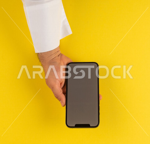 صورة مقربة ليد رجل عربي خليجي سعودي يستخدم الهاتف المحمول ،ايماءات اليد تدل على عرض مواصفات الجهاز المحمول ،الترويج لتطبيق الكتروني ، التسويق لموقع ويب ، اجراء مكالمات فيديو
