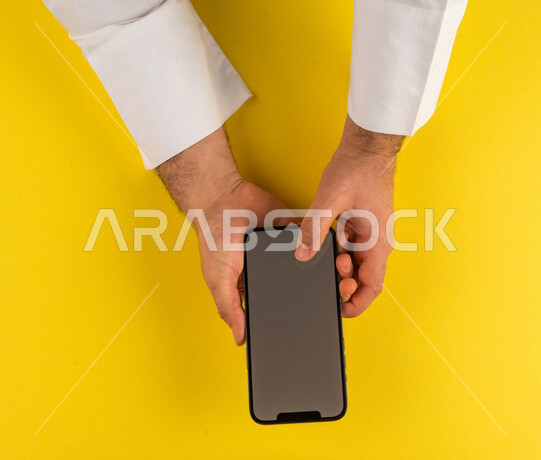 صورة مقربة ليد رجل عربي خليجي سعودي ينقر على شاشة الهاتف المحمول ، التسويق الالكتروني، تصفح المواقع الالكترونية ،تحديد الموقع ، العاب الكترونية ،ستخدام الاجهزة التقنية الحديثة في الاعمال الادارية