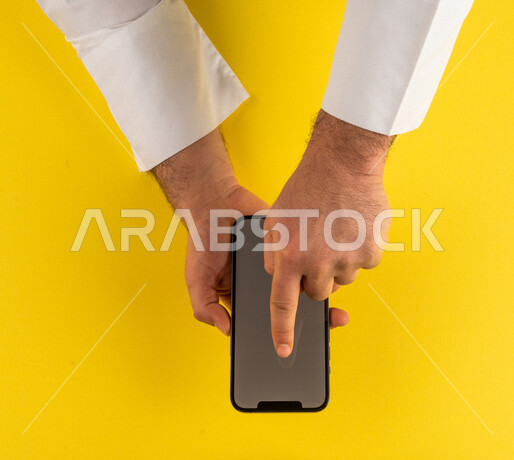 صورة مقربة ليد رجل عربي خليجي سعودي ينقر على شاشة الهاتف المحمول ، التسويق الالكتروني، تصفح المواقع الالكترونية ،تحديد الموقع ، العاب الكترونية ،ستخدام الاجهزة التقنية الحديثة في الاعمال الادارية