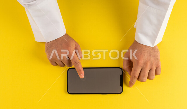 صورة مقربة ليد رجل عربي خليجي سعودي ينقر على شاشة الهاتف المحمول ، التسويق الالكتروني، تصفح المواقع الالكترونية ،تحديد الموقع ، العاب الكترونية ،ستخدام الاجهزة التقنية الحديثة في الاعمال الادارية