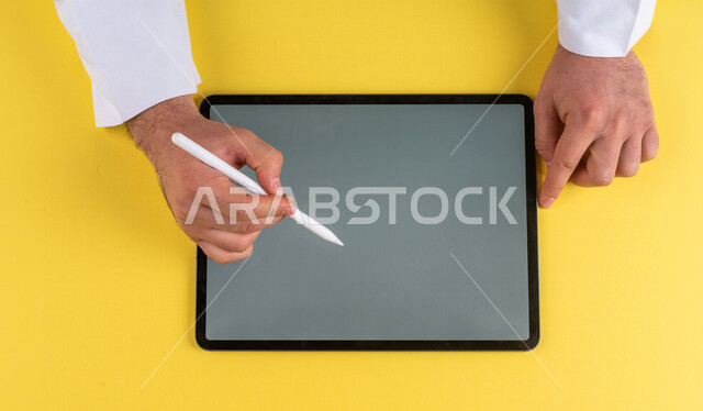 A close-up of the hand of a Saudi Arabian Gulf man using a tablet device, using a tablet pen to take notes on work, explaining work steps, marketing for a website, drawing pictures and designs, using modern technologies in administrative work