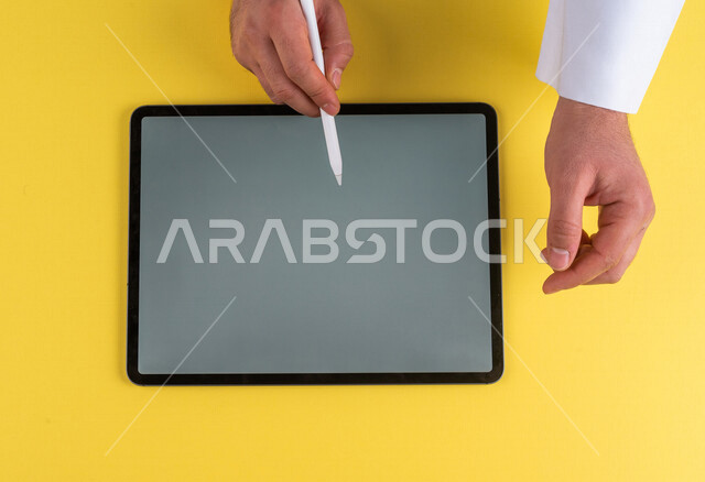 صورة مقربة ليد رجل عربي خليجي سعودي يستخدم جهاز التابلت ، استخدام قلم التابلت لتدوين ملاحظات خاصة بالعمل ،شرح خطوات العمل ، التسويق لموقع الكتروني ،رسم الصور والتصاميم ،استخدام التقنيات الحديثة في الاعمال الادارية
