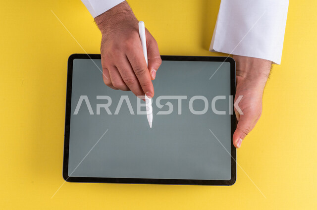 صورة مقربة ليد رجل عربي خليجي سعودي يستخدم جهاز التابلت ، استخدام قلم التابلت لتدوين ملاحظات خاصة بالعمل ،شرح خطوات العمل ، التسويق لموقع الكتروني ،رسم الصور والتصاميم ،استخدام التقنيات الحديثة في الاعمال الادارية