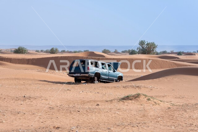 سيارة زرقاء مهجورة وسط الصحراء بالمملكة العربية السعودية، الكثبان والتلال الرملية في المناطق الصحراوية، التشكيلات والتكوينات الصخرية، مغامرات ورحلات في الصحاري الواسعة، التضاريس القاسية والطبيعة الجبلية، الرمال الذهبية اللامعة في النهار