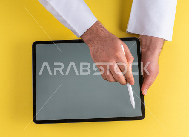 صورة مقربة ليد رجل عربي خليجي سعودي يستخدم جهاز التابلت ، استخدام قلم التابلت لتدوين ملاحظات خاصة بالعمل ،شرح خطوات العمل ، التسويق لموقع الكتروني ،رسم الصور والتصاميم ،استخدام التقنيات الحديثة في الاعمال الادارية