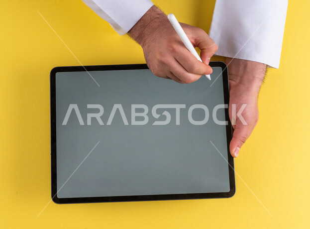 صورة مقربة ليد رجل عربي خليجي سعودي يستخدم جهاز التابلت ، استخدام قلم التابلت لتدوين ملاحظات خاصة بالعمل ،شرح خطوات العمل ، التسويق لموقع الكتروني ،رسم الصور والتصاميم ،استخدام التقنيات الحديثة في الاعمال الادارية