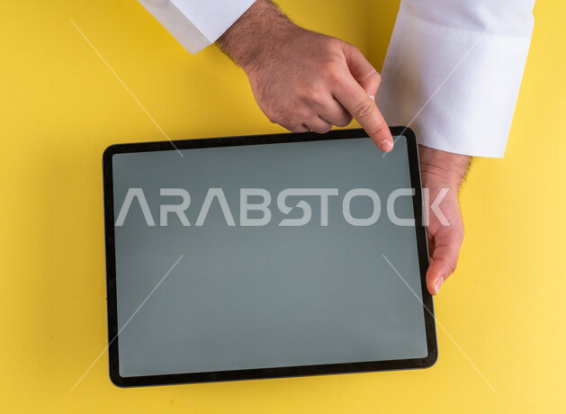 صورة مقربة ليد رجل عربي خليجي سعودي ينقر على شاشة جهاز التابلت، شرح خطوات العمل ،القيام بعمليات التسويق الالكتروني ، التجارة الالكترونية ،تصفح المواقع الالكترونية ، استخدام الاجهزة التقنية الحديثة في الاعمال الادارية