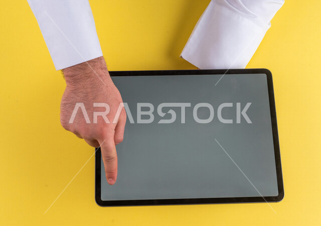 صورة مقربة ليد رجل عربي خليجي سعودي ينقر على شاشة جهاز التابلت، شرح خطوات العمل ،القيام بعمليات التسويق الالكتروني ، التجارة الالكترونية ،تصفح المواقع الالكترونية ، استخدام الاجهزة التقنية الحديثة في الاعمال الادارية