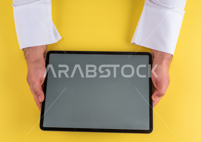 صورة مقربة ليد رجل عربي خليجي سعودي يستخدم جهاز التابلت، الاستمتاع بمشاهدة الافلام ، لعب الالعاب الالكترونية ، متابعة الدروس التعليمية ،استخدام التقنيات الحديثة