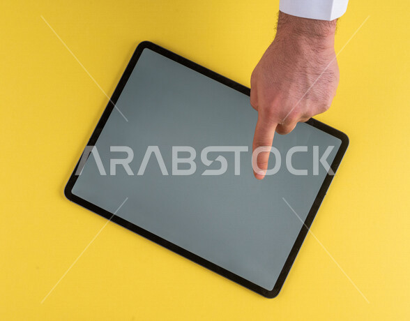 صورة مقربة ليد رجل عربي خليجي سعودي ينقر على شاشة جهاز التابلت، شرح خطوات العمل ،القيام بعمليات التسويق الالكتروني ، التجارة الالكترونية ،تصفح المواقع الالكترونية ، استخدام الاجهزة التقنية الحديثة في الاعمال الادارية
