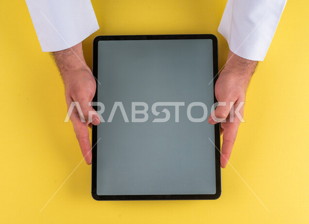صورة مقربة ليد رجل عربي خليجي سعودي يستخدم جهاز التابلت، الاستمتاع بمشاهدة الافلام ، لعب الالعاب الالكترونية ، متابعة الدروس التعليمية ،استخدام التقنيات الحديثة