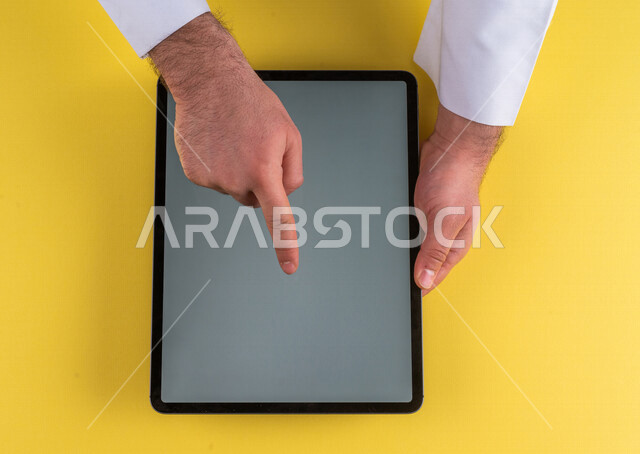 صورة مقربة ليد رجل عربي خليجي سعودي ينقر على شاشة جهاز التابلت، شرح خطوات العمل ،القيام بعمليات التسويق الالكتروني ، التجارة الالكترونية ،تصفح المواقع الالكترونية ، استخدام الاجهزة التقنية الحديثة في الاعمال الادارية