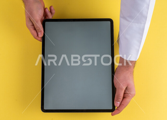 صورة مقربة ليد رجل عربي خليجي سعودي يستخدم جهاز التابلت، الاستمتاع بمشاهدة الافلام ، لعب الالعاب الالكترونية ، متابعة الدروس التعليمية ،استخدام التقنيات الحديثة
