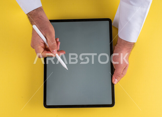 A close-up of the hand of a Saudi Arabian Gulf man using a tablet device, using a tablet pen to take notes on work, explaining work steps, marketing for a website, drawing pictures and designs, using modern technologies in administrative work