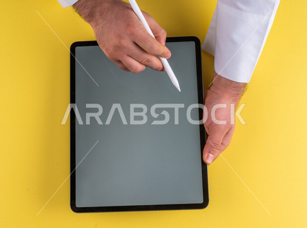 A close-up of the hand of a Saudi Arabian Gulf man using a tablet device, using a tablet pen to take notes on work, explaining work steps, marketing for a website, drawing pictures and designs, using modern technologies in administrative work
