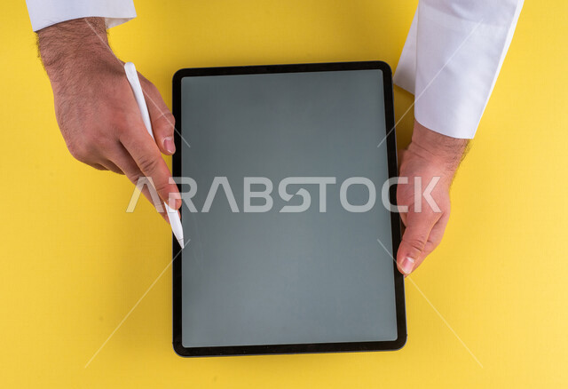 صورة مقربة ليد رجل عربي خليجي سعودي يستخدم جهاز التابلت ، استخدام قلم التابلت لتدوين ملاحظات خاصة بالعمل ،شرح خطوات العمل ، التسويق لموقع الكتروني ،رسم الصور والتصاميم ،استخدام التقنيات الحديثة في الاعمال الادارية