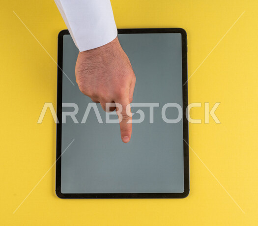 صورة مقربة ليد رجل عربي خليجي سعودي ينقر على شاشة جهاز التابلت، شرح خطوات العمل ،القيام بعمليات التسويق الالكتروني ، التجارة الالكترونية ،تصفح المواقع الالكترونية ، استخدام الاجهزة التقنية الحديثة في الاعمال الادارية