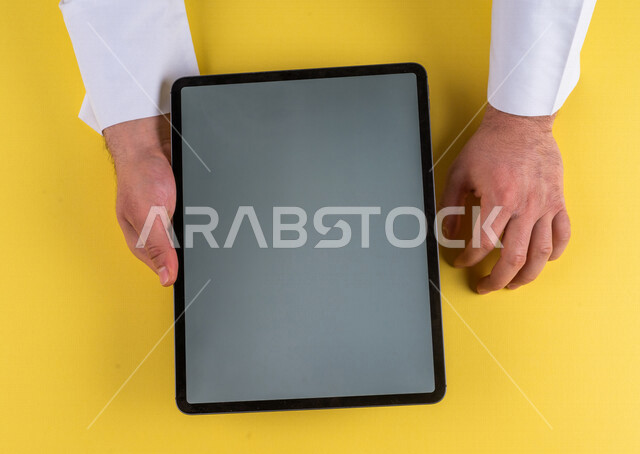 صورة مقربة ليد رجل عربي خليجي سعودي يستخدم جهاز التابلت، الاستمتاع بمشاهدة الافلام ، لعب الالعاب الالكترونية ، متابعة الدروس التعليمية ،استخدام التقنيات الحديثة