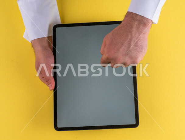 صورة مقربة ليد رجل عربي خليجي سعودي ينقر على شاشة جهاز التابلت، شرح خطوات العمل ،القيام بعمليات التسويق الالكتروني ، التجارة الالكترونية ،تصفح المواقع الالكترونية ، استخدام الاجهزة التقنية الحديثة في الاعمال الادارية