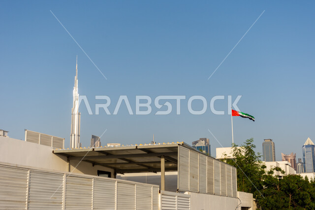 برج خليفة في مدينة دبي في وقت النهار, العلم الإماراتي يرفرف في سماء منطقة جميرا, الأماكن السياحية المشهورة في الإمارات العربية المتحدة, جذب واستقطاب السياح من أنحاء العالم, الفن الهندسي المعماري لبناء الأبراج وناطحات السحاب