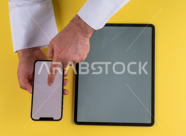 صورة مقربة ليد رجل عربي خليجي سعودي ينقر على شاشة الهاتف المحمول ، استخدام جهاز التابلت، التسويق الالكتروني للتطبيقات، التجارة الالكترونية  ، استخدام الاجهزة التقنية الحديثة في الاعمال الادارية