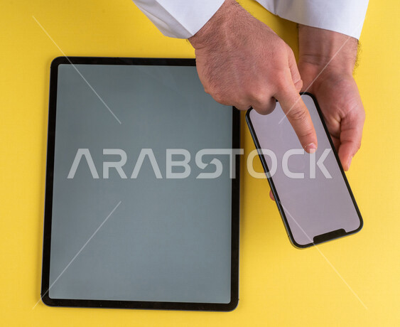 صورة مقربة ليد رجل عربي خليجي سعودي ينقر على شاشة الهاتف المحمول ، استخدام جهاز التابلت، التسويق الالكتروني للتطبيقات، التجارة الالكترونية  ، استخدام الاجهزة التقنية الحديثة في الاعمال الادارية