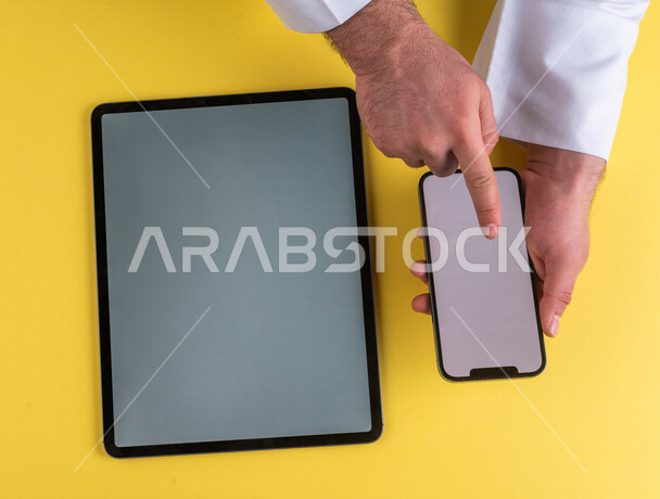 A close-up of the hand of a Saudi Arabian Gulf man clicking on a mobile phone screen, using a tablet device, e-marketing for applications, e-commerce, using modern technical devices in administrative work