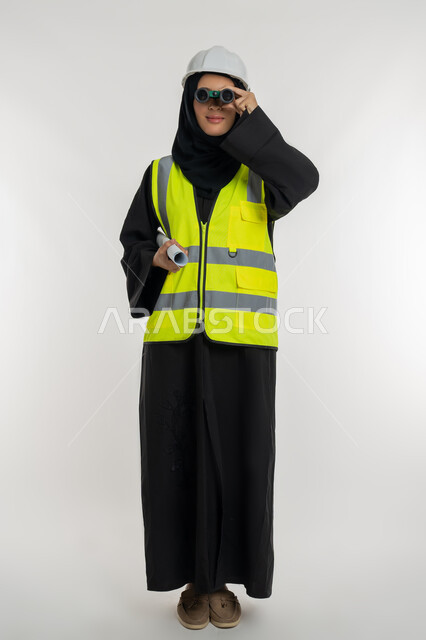 التطلع للاهداف المستقبلية، العمل في القطاع الهندسي، حب المغامرة والاستكشاف، مخططات و مشاريع اعمارية، بورتريه لامرأة عربية خليجية سعودية محجبة مبتسمة تحمل بيدها مخطط المشروع، شابة سعودية تنظر من خلال منظار ثنائي العينين، صورة لكامل الجسم، خلفية بيضاء