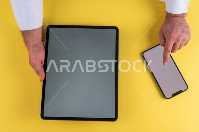 A close-up of the hand of a Saudi Arabian Gulf man clicking on a mobile phone screen, using a tablet device, e-marketing for applications, e-commerce, using modern technical devices in administrative work