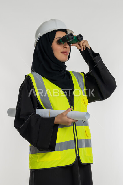العمل في القطاع الهندسي، حب المغامرة والاستكشاف، التطلع للاهداف المستقبلية، مخططات و مشاريع اعمارية، بورتريه لامرأة عربية خليجية سعودية محجبة مبتسمة تحمل بيدها مخطط المشروع، شابة سعودية تنظر من خلال منظار ثنائي العينين، خلفية بيضاء