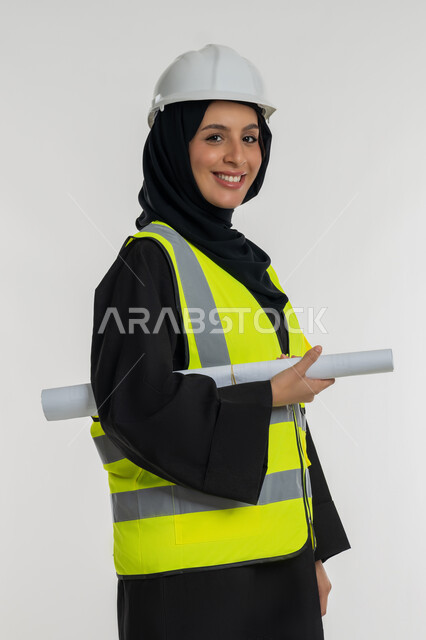 تعابير السرور والسعادة، العمل في القطاع الهندسي، مخططات و مشاريع اعمارية، مهن ووظائف نسائية هندسية، بورتريه من الجانب لامرأة عربية خليجية سعودية محجبة مبتسمة تحمل بيدها مخطط المشروع، شابة سعودية تقوم بالاشراف على العمل، خلفية بيضاء