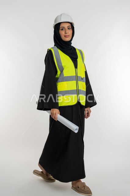 مهن ووظائف هندسية، ايماءات السير والتوجه لمكان ما، العمل في القطاع الهندسي، مخططات و مشاريع اعمارية، بورتريه لامرأة عربية خليجية سعودية محجبة مبتسمة تحمل بيدها مخطط المشروع، شابة سعودية تقوم بالاشراف على العمل، خلفية بيضاء