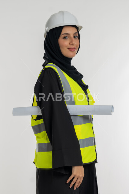 ايماءات السرور والسعادة، العمل في القطاع الهندسي، مخططات و مشاريع اعمارية، مهن ووظائف نسائية هندسية، بورتريه من الجانب لامرأة عربية خليجية سعودية محجبة مبتسمة تحمل بيدها مخطط المشروع، شابة سعودية تقوم بالاشراف على العمل، خلفية بيضاء