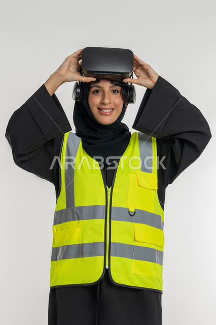 Developing engineering fields through VR glasses, future vision 2030, integration with virtual engineering, portrait of an Arab Gulf Emirati female engineer wearing a protective jacket and helmet, putting on virtual reality glasses, a young Saudi woman looking at the camera with gestures of pleasure, white background