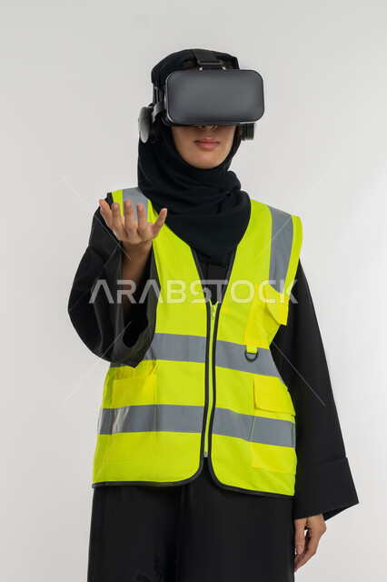 Future vision 2030, developing engineering fields through VR glasses, interacting with virtual engineering, portrait of an Arab Gulf Emirati female engineer wearing a protective jacket and helmet, putting on virtual reality glasses, a young Saudi woman raising her hand with gestures of carrying an item, white background