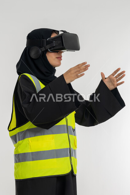 Developing engineering fields through VR glasses, expressions of holding an item, interacting with virtual engineering, close-up portrait from the side of an Arab Gulf Emirati female engineer wearing a protective jacket and helmet, putting on virtual reality glasses, a young Saudi woman raising her hands with scaling gestures, white background