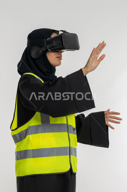 Interacting with virtual engineering, developing engineering fields through VR glasses, close-up portrait from the side of an Arab Gulf Emirati female engineer wearing a protective jacket and helmet, wearing virtual reality glasses, a young Saudi woman raising her hands with gestures of integration, white background