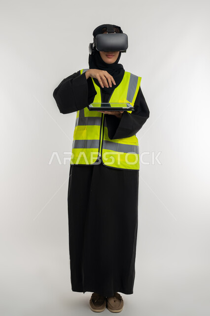 The concept of interacting with virtual engineering, developing engineering fields through VR glasses, portrait of an Arab Gulf Emirati female engineer wearing a protective jacket and helmet, wearing virtual reality glasses and holding a tablet, a young Saudi woman raising her hands with gestures of integration, full body image, white background