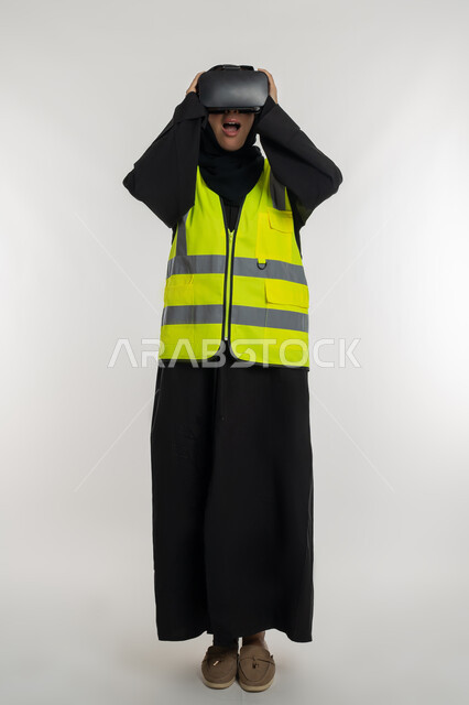 رؤية مستقبلية 2030 ، تطوير المجالات الهندسية عبر نظارات الفي آر، الاندماج مع الهندسة الافتراضية، بورتريه لمهندسة عربية خليجية اماراتية ترتدي سترة وخوذة الحماية تضع نظارة الواقع الافتراضي، شابة سعودية تمسك النظارات بايماءات الدهشة، صورة لكامل الجسم، خلفية بيضاء