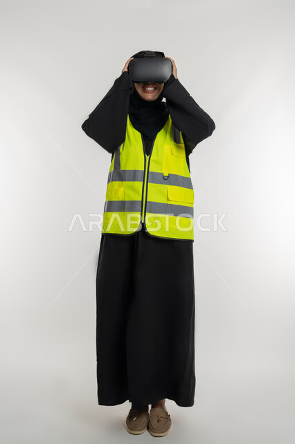 Developing engineering fields through VR glasses, future vision 2030, integration with virtual engineering, portrait of an Arab Gulf Emirati female engineer wearing a protective jacket and helmet, putting on virtual reality glasses, a young Saudi woman holding glasses with gestures of pleasure, full body image, white background