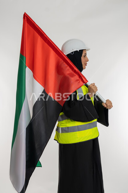 الاحتفال بيوم العلم الاماراتي 3 نوفمبر، ذكرى يوم الاستقلال 2 ديسمبر، بورتريه من الجانب لمهندسة عربية خليجية اماراتية ترتدي سترة وخوذة الحماية تحمل بيدها علم دولة الإمارات المتحدة، إيماءات الفخر والإعتزاز بالانتماء للوطن، خلفية بيضاء