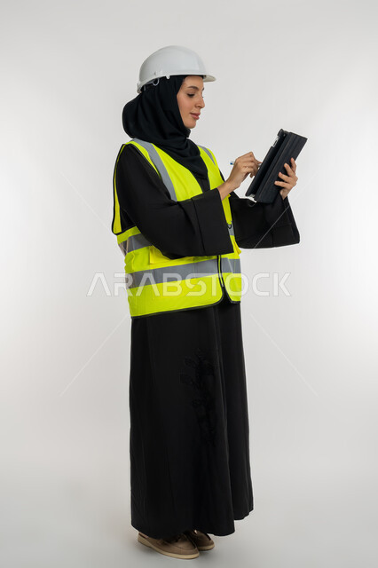 Working in the engineering sector, engineering project management, remote task completion, portrait of the side of an Emirati Arab-Gulf engineer wearing a jacket and protection helmet working on the tablet, a young Saudi woman studying the basics of the project, a picture of the whole body, white background