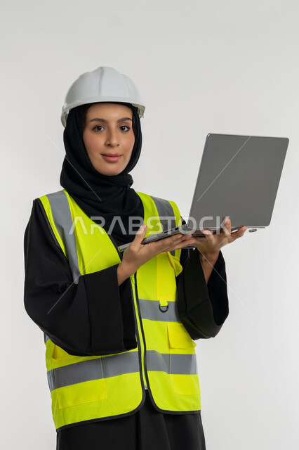 Completing work tasks via laptop, portrait of an Arab Gulf Emirati female engineer wearing a protective jacket and helmet holding a laptop, engineering project management, working in the engineering sector, a young Saudi woman studying the basics of the project, white background